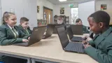 A group of school children sat at a desk with laptops